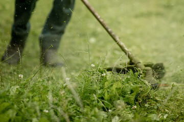 Worker with a gas mower in his hands, mowing grass in front of the house. Trimmer in the hands of a...