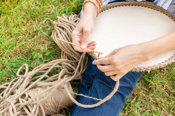 Woman is crocheting a basket from a thick cord from eco friendly materials and wood bottom, on the...