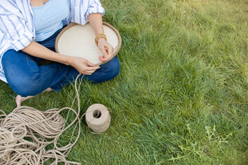 Girl knits a crochet basket on the grass, sitting in the garden on the grass. Hobby at home.