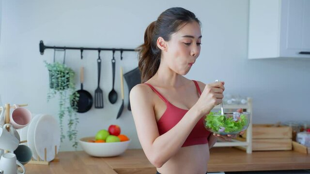 Asian attractive sport woman holding salad bowl and eat vegetables.