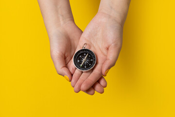 Close-up female hands holding a compass on a yellow background. Travel lifestyle, summer vacation concept