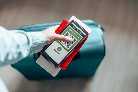 Traveler Holding A Passport, Ticket Pass And Smartphone With Digital Health Passport App For Travel During Covid-19 Pandemic.