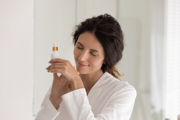 Peaceful happy young woman applying oil perfume on hands, enjoying pleasant aroma fragrance....