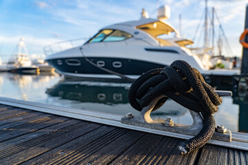 Closeup picture a rope tied to a metal cleat on a yacht deck with boat on background 