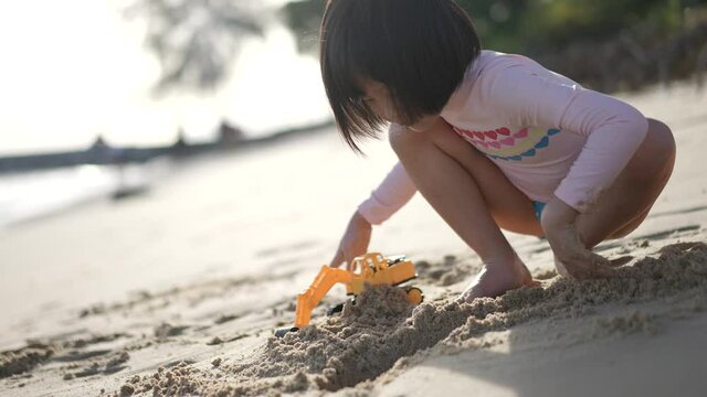 Slow motion of little asian chinese girl digging sand at the beach with her excavator outdoor sunny