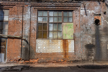 A large old dilapidated house made of colorful bricks with large dilapidated windows and a wooden door. Old dirty abandoned factory building.