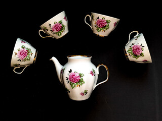 Tea set: four white mugs and a teapot in white with a flower on a black background