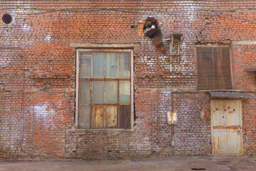 Fototapeta na wymiar A large old dilapidated red brick house with a rusty window and a metal door. Old dirty abandoned factory building.
