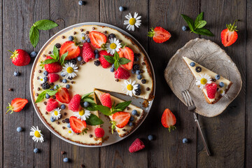 Slice of cheesecake, classic New York style cheesecake decorated with strawberries, blueberries, blackberries and mint on a wooden background. Piece of delicious cake on a white plate
