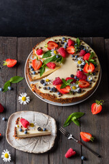 Slice of cheesecake, classic New York style cheesecake decorated with strawberries, blueberries, blackberries and mint on a wooden background. Piece of delicious cake on a white plate
