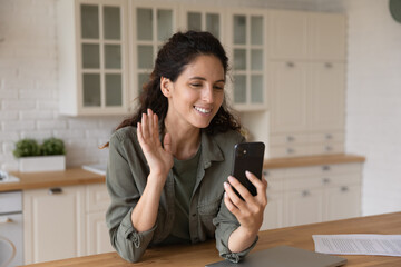 Happy young hispanic woman waving hand, starting distant video call mobile meeting, enjoying communicating remotely with friends or family. Smiling attractive female blogger recording video stories.