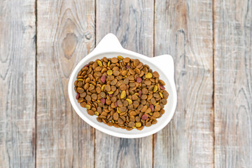 Cat head bowl with dry food on wooden background with copyspace. Healthy pet diet nutrition, feline feed choice, domestic animals dinner time. Top view.