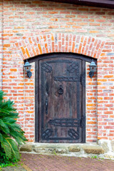 The facade of a vintage carved doorway, old wooden doors with a lock and a ring doorknock and street light on brick wall, antique building entry.