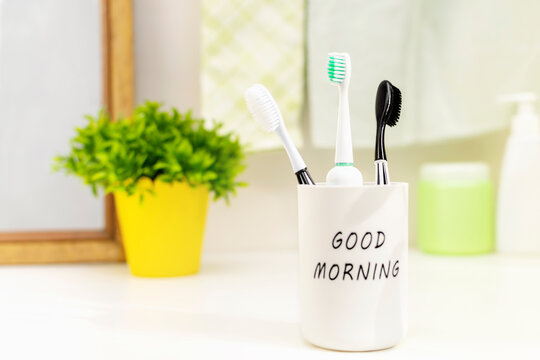 Three family toothbrushes stand in a white glass on the bathroom counter at a sunny good morning. The concept of daily dental hygiene, routine and oral care and the prevention of caries.