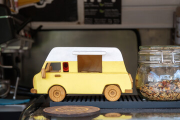 Yellow toy vintage van on food truck counter. Wooden model of retro car in mobile coffee shop.