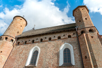 Fototapeta na wymiar A beautiful old fortress church made of red brick against a blue sky background. A high impregnable fortress with iron crosses on the domes, arched windows and an icon in the center of the wall.