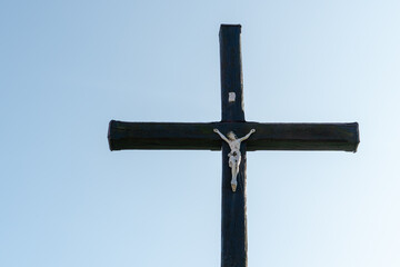 An old wooden Christian cross against a clear blue sky on a beautiful summer day. A statuette of...