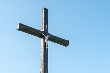 An old wooden Christian cross against a clear blue sky on a beautiful summer day. A statuette of...