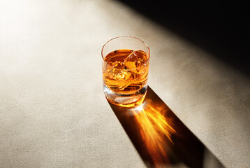 Glass of elegant whiskey with ice cubes on a bar counter with dark moody atmosphere.