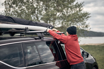 Windsurfer and camper packing and unpacking from a car's roof rack in nature.