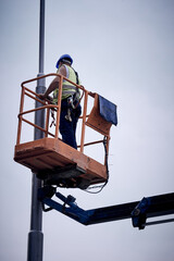 Manual worker on a telescopic lifter basket fixing street light pole.