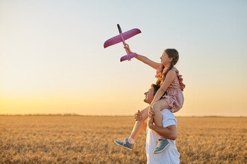 girl riding on father's shoulder and playing with toy airplane