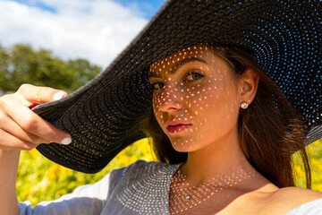 closeup portrait of woman in elegant hat enjoying summer sun, pattern of shadows falling on her face