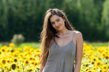 young woman with long hair in linean country style dress walks through a field of sunflowers