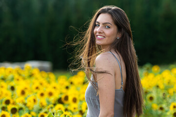 Naklejka na ściany i meble young woman with long hair in linean country style dress walks through a field of sunflowers