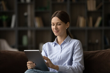 Close up woman using tablet, sitting on cozy couch at home, attractive young female looking at device screen, typing writing message in social network, browsing apps, shopping or chatting online