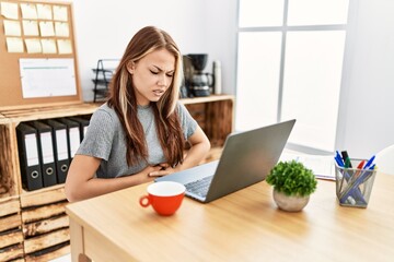 Young brunette woman working at the office with laptop with hand on stomach because indigestion,...