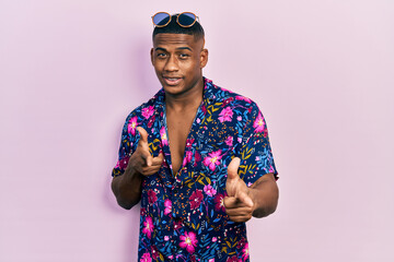 Young black man wearing hawaiian shirt and sunglasses pointing fingers to camera with happy and...
