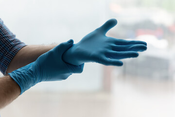 Hands of man putting on blue latex rubber gloves for household works, protecting skin from water, caring for hygiene and virus spread prevention during coronavirus pandemic, outbreak