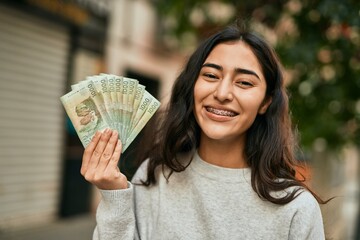 Young middle east girl smiling happy holding chile pesos banknotes at the city.