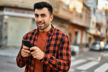 Young hispanic man smiling happy using smartphone at the city.