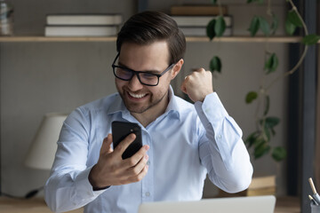 Excited mobile phone user enjoying win, celebrating success, achieve, high job result. Happy businessman using smartphone, reading text message, feeling joy, euphoria, making hand winner gesture