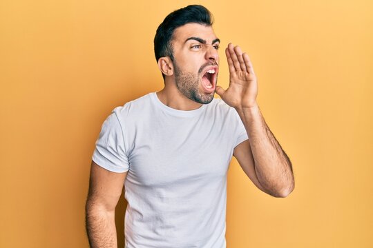 Young hispanic man wearing casual white t shirt shouting and screaming loud to side with hand on mouth. communication concept.