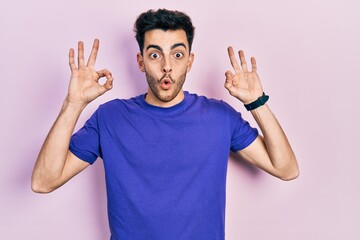 Fototapeta premium Young hispanic man wearing casual t shirt looking surprised and shocked doing ok approval symbol with fingers. crazy expression