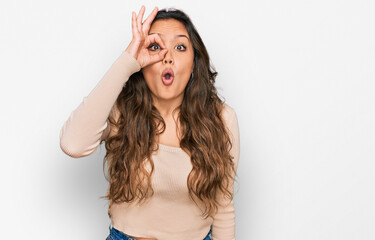 Naklejka premium Young hispanic girl wearing casual clothes doing ok gesture shocked with surprised face, eye looking through fingers. unbelieving expression.