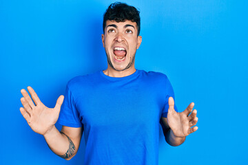 Young hispanic man wearing casual blue t shirt crazy and mad shouting and yelling with aggressive expression and arms raised. frustration concept.