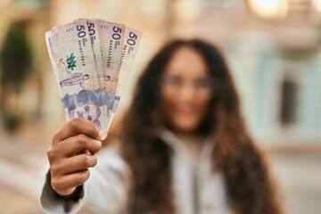 Young latin woman smiling happy holding colombia pesos banknotes at the city.