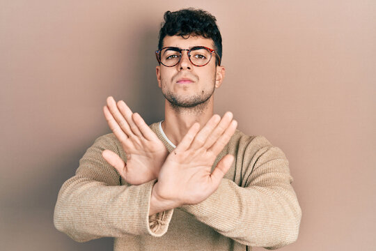 Young hispanic man wearing casual clothes and glasses rejection expression crossing arms doing negative sign, angry face