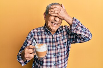 Handsome senior man with grey hair drinking a cup coffee smiling and laughing with hand on face covering eyes for surprise. blind concept.