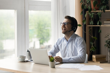 Obraz premium Happy excited businessman in headphones working at laptop, watching learning webinar, online virtual training. Contact center employee, sales manager having funny video call, laughing at workplace
