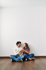 Young hispanic couple toasting with champagne sitting on the floor at empty new home.