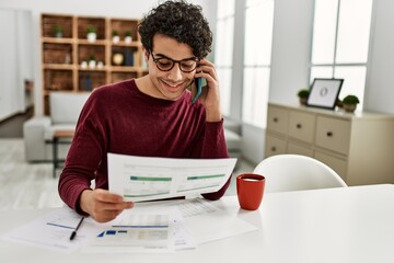 Young hispanic man talking on the smartphone working at home.