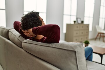 Young hispanic man on back view relaxing with hands on head sitting on the sofa at home.