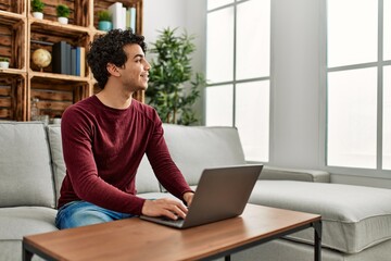 Young hispanic man using laptop sitting on the sofa at home.