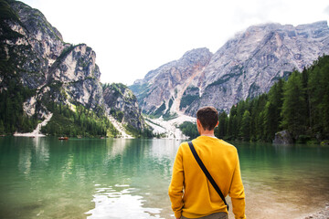 Young guy in a yellow sweatshirt standing in front of the lago di Braies in the Dolomites of South Tyrol. Tourism direction to northern Italy. Bolzano Lago di Braies 