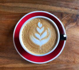 Flat white. Top view of hot coffee (cappuccino or latte) in red cup over brown wooden rustic background.